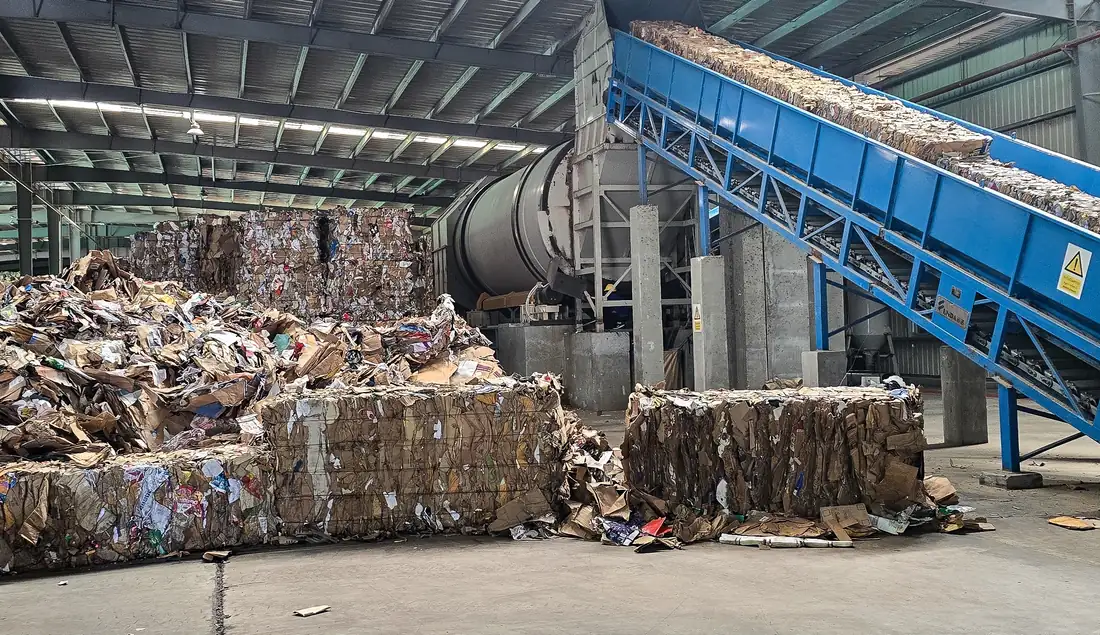 Baled paper waste and conveyor in an industrial paper recycling facility